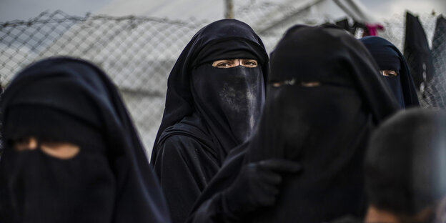 Frauen in Niqab stehen vor einem Maschendrahtzaun