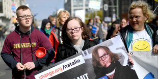 Drei Personen tragen ein Plakat auf einer Demonstration