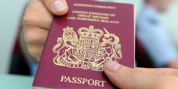 Eine Hand überreicht einer anderen Hand einen dunkelroten britischen Reisepass