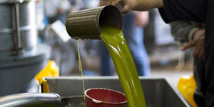 Eine Hand schüttet Olivenöl in einen Behälter
