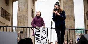 Zwei junge Frauen stehen vor dem Brandenburger Tor, eine spricht in ein Mikrofon