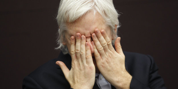 Julian Assange hält sich die Hände vor das Gesicht, das Bild zeigt ihn im Jahr 2011.