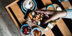 Foto eines Smartphones, das einen Tisch voller Essen fotografiert, der ebenfalls zu sehen