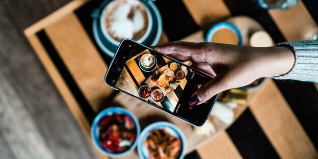 Foto eines Smartphones, das einen Tisch voller Essen fotografiert, der ebenfalls zu sehen