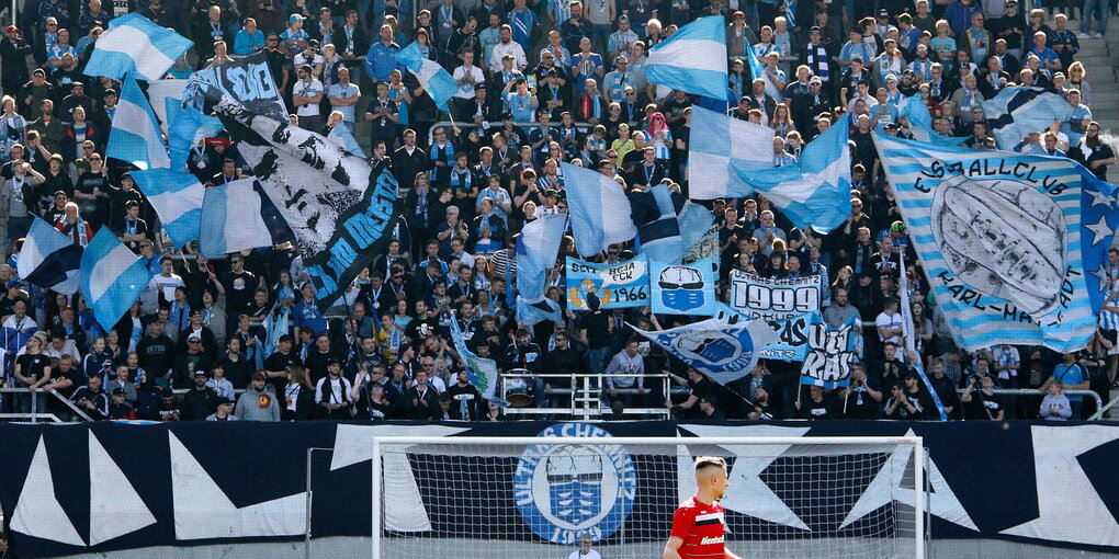 auf einer vollen Tribühne schwenken Fans blau-weiße Fahnen