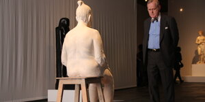 Ein Mann im Anzug betrachtet eine weiße Skulptur einer Mutter