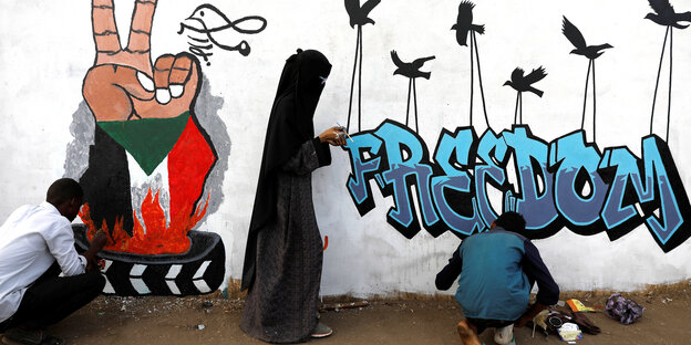 Drei Menschen arbeiten an einem Graffiti an einer Wand