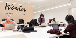 Frauen in einem Büro vor ihren aufgeklappten Macbooks. An der Wand steht Wonder Womens Coworking.