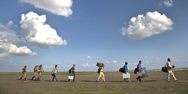 Menschen in wüstenartiger Landschaft mit schwerem Gepäck