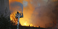 Feuerwehrmann auf einer Leiter vor hohen Flammen