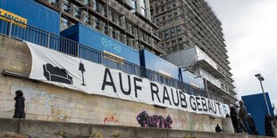 An einem Neubau hängt ein Transparent mit der Aufschrift "Auf Raub gebaut".