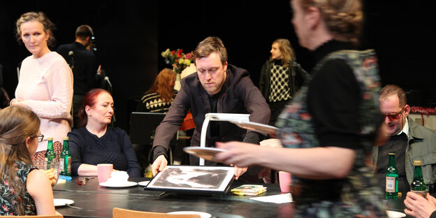 Der Knausgård-Darsteller Robin Sondermann inmitten von Menschen an einem Tisch.