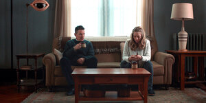 Ein Mann und eine Frau sitzen im Halbdunkel in einem Wohnzimmer.