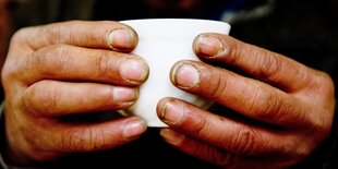 Ein obdachloser Mann hält in einem Nachtcafé eine Tasse.