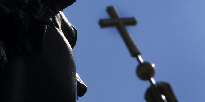 Vor blauem Himmel zeichnen sich die Statue "Kämpfende Amazone" vor dem Kuppelkreuz des Berliner Doms ab.