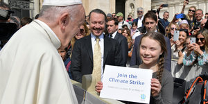 Ein Mädchen hält ein Plakat und grinst. Sie guckt den Papst an