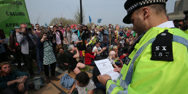 Ein Polizist verkündet den Demonstranten die Gesetzeslage zur öffentlichen Ordnung bei einem Klimaprotest