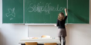 Eine Frau schreibt das Wort "Schulfrieden" auf eine Tafel