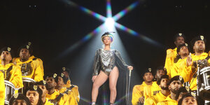 Beyoncé auf der Bühne. Rechts und links Musiker in gelben Pullis.