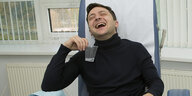 Wladimir Selenski in einem medizinischen Behandlungszimmer. Er lacht. Neben ihm steht ein Mann in weißen Kittel.