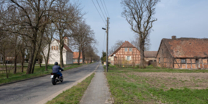 Ein Motorrad fährt auf einer Dorfstraße vor Fachwerkhäusern