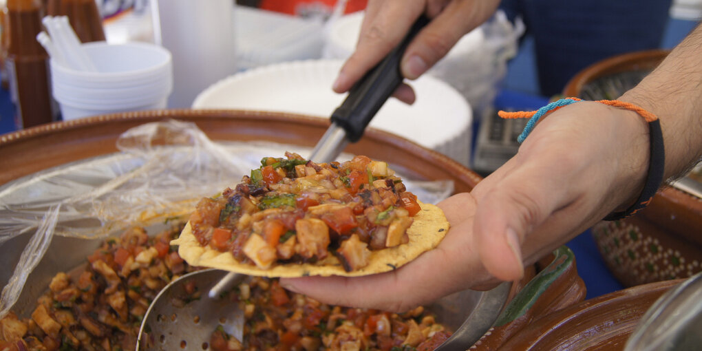 Ein Taco liegt auf einer Hand, es wird gerade gefüllt