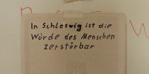 Auf einem Pappteller steht "In Schleswig ist die Würde des Menschen zerstörbar".