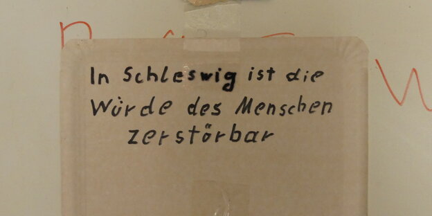 Auf einem Pappteller steht "In Schleswig ist die Würde des Menschen zerstörbar".