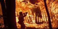 Ein feuerwehrmann trägt einen Löschschlauch zu einem brennenden Haus