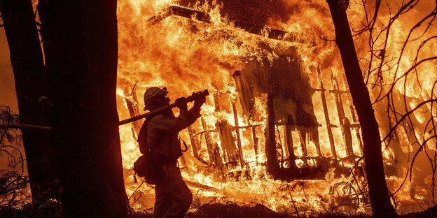 Ein feuerwehrmann trägt einen Löschschlauch zu einem brennenden Haus