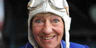 Heidi Hetzer lacht und trägt eine Rallye-Mütze aus Leder mit einer auf die Stirn geschobenen Windschutzbrille.