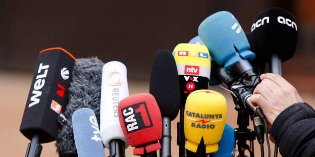 Mikrofone von diversen deutschen und internationalen Medien, davor eine Hand, die ein Mikrofon einrichtet
