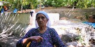 Eine ältere Frau sitzt auf einem baufälligen Grundstück