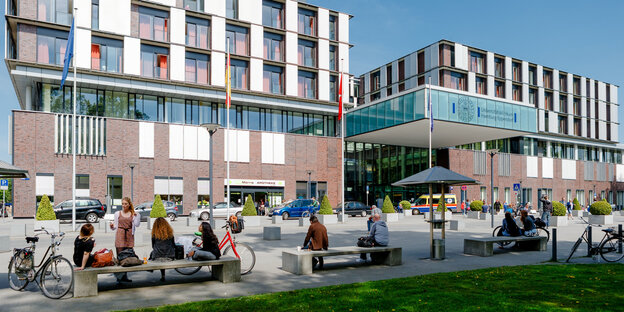 Menschen sitzen auf Bänken vor dem Haupteingang des Universitätsklinikums Eppendorf.