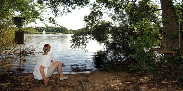 Eine junge Frau sitzt am Ufer der Süderelbe im Naturschutzgebiet Heuckenlock in Hamburg-Wilhelmsburg.
