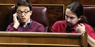 Íñigo Errejón telefoniert und Pablo Iglesias schaut genervt, beide sitzen nebeneinander auf der Abgeordnetenbank