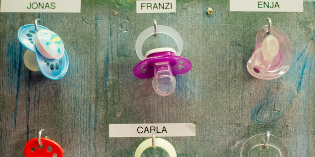 Schnuller hängen an beschrifteten Haken. Ein blauer für "Jonas" und pinke für "Carla" und "Enja"
