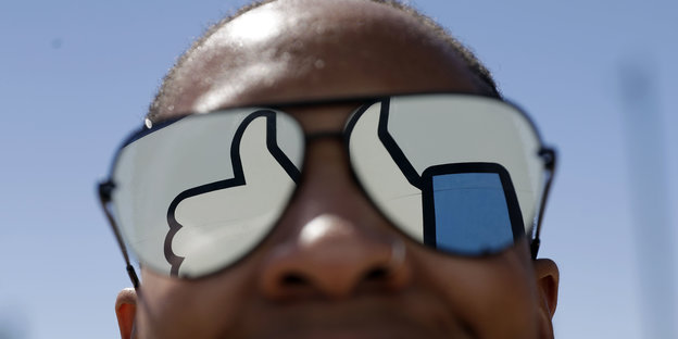 In einer Sonnenbrille spiegelt sich der Facebook-Daumen