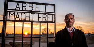 Axel Drecoll steht neben einem Gittertorm it der Inschrift ,Arbeit macht frei'