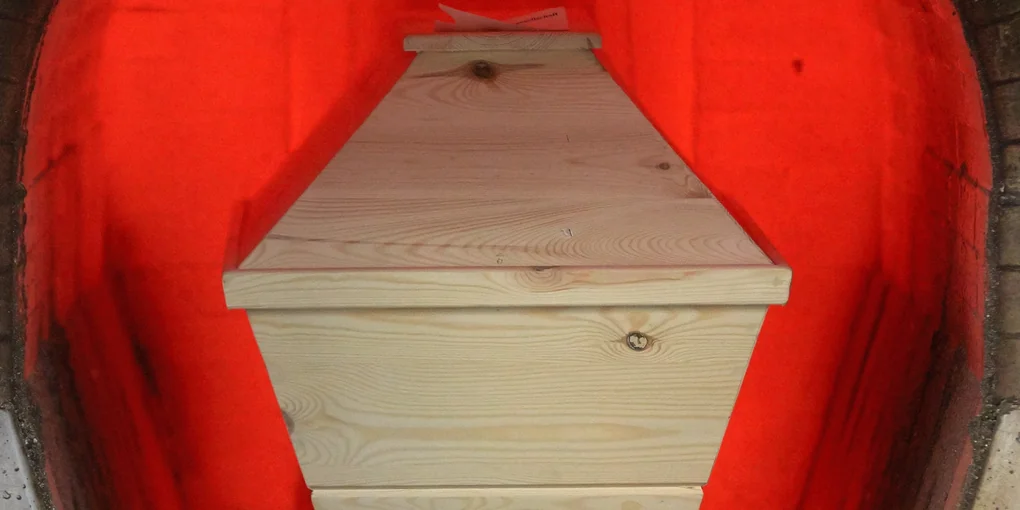 Ein Holzsarg, der ins Krematorium geschoben wird
