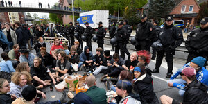 Leute sitzen auf dem Boden, dahinter stehen Polizisten