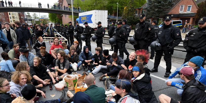 Leute sitzen auf dem Boden, dahinter stehen Polizisten