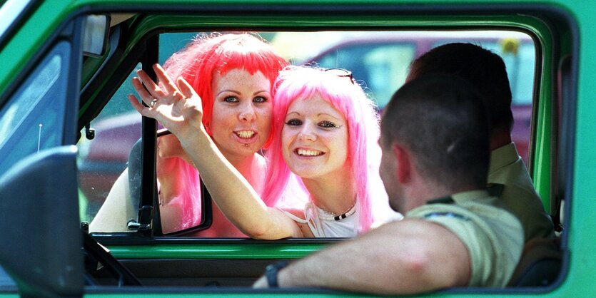 2 Frauen mit roten Perrücken gucken in ein Polizeiauto