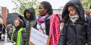 Trauernde Menschen der afrikanischen Community Hamburgs bei Trauerfeier für den verstorbenenTonou Mbobda halten Plakate mit der Aufschrift "Wir fordern Gerechtigkeit".