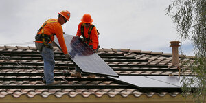Zwei behelmte Männer stehen auf einem Dach und verlegen Solarzellen