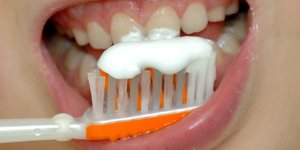 Nahaufnahme einer Zahnbürste mit Zahnpasta, die vor einen Kindermund gehalten wird.