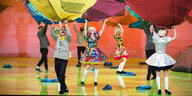 Bunt kostümierte Schauspieler halten aufgespannte Zelte über sich wie verdrehte Regenschirme