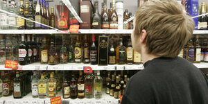 Ein Junge steht in einem Supermarkt vor einem Spirituosenregal
