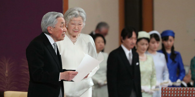 Der Kaiser von Japan steht mit seiner Frau und liest eine Rede vom Blatt
