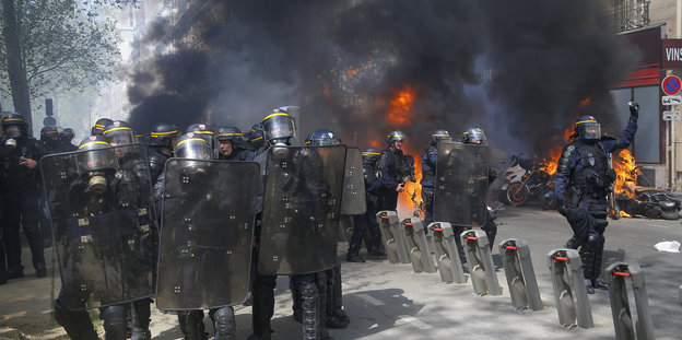 Polizisten in Kampfmontur vor brennenden Motorrädern